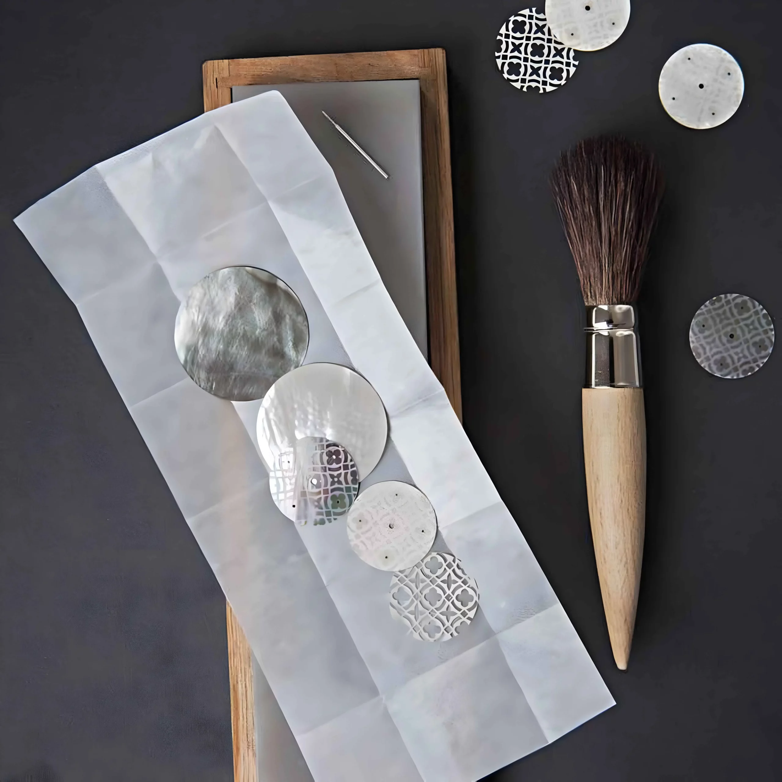 a brush and paper with watch mother of pearls dials on it